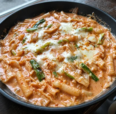 Rose ddeokbokki rice cakes and fish cake in a creamy pink chili sauce with melted cheese and green onion